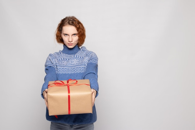 Chica joven en un suéter sostiene un regalo sobre un fondo blanco.