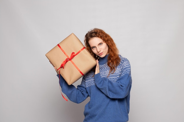 Foto chica joven en un suéter sostiene un regalo sobre un fondo blanco.