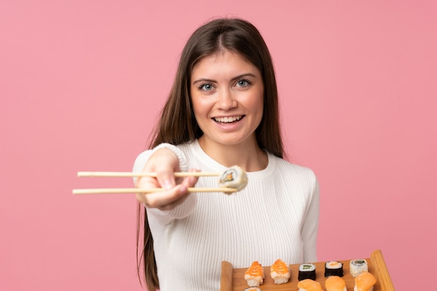 Chica joven con sushi sobre pared rosa aislado