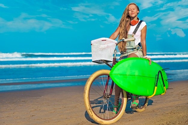 Chica joven con tabla de surf y bicicleta en la playa