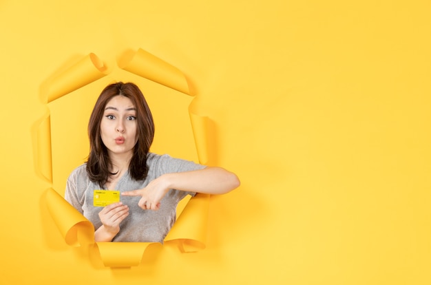 Chica joven con tarjeta de crédito mirando a través de la ventana de venta de fondo de papel amarillo rasgado