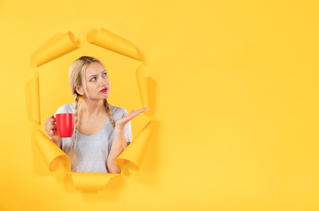 Chica joven con una taza de té sobre fondo de papel amarillo rasgado publicidad tratamientos faciales de compras