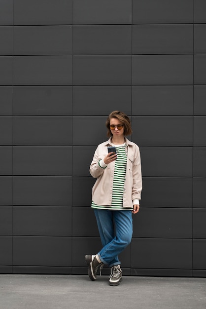 Foto chica joven con teléfono inteligente al aire libre retrato fondo de pared gris