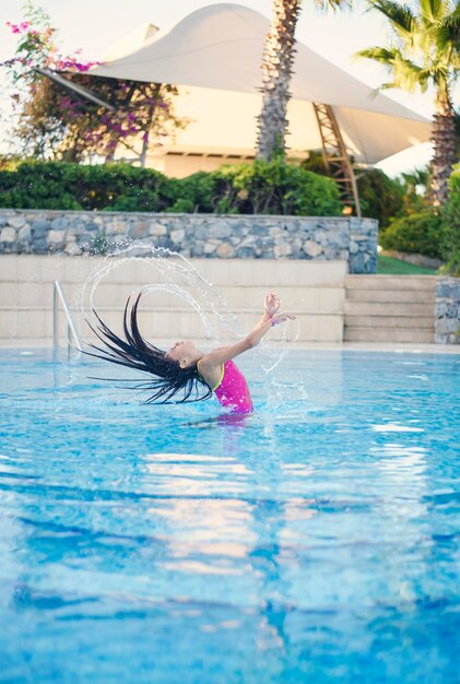 Chica joven con traje de baño rosa emerge de la piscina salpica su cabello