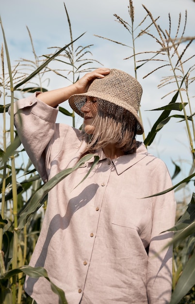 Chica joven en un traje de lino y un sombrero en un día soleado de verano se encuentra en un campo de maíz el amor por los viajes y