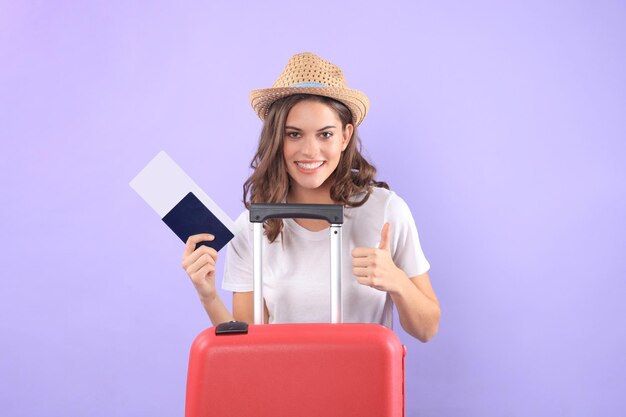 Chica joven turista en ropa casual de verano, con gafas de sol, maleta roja, pasaporte aislado sobre fondo púrpura