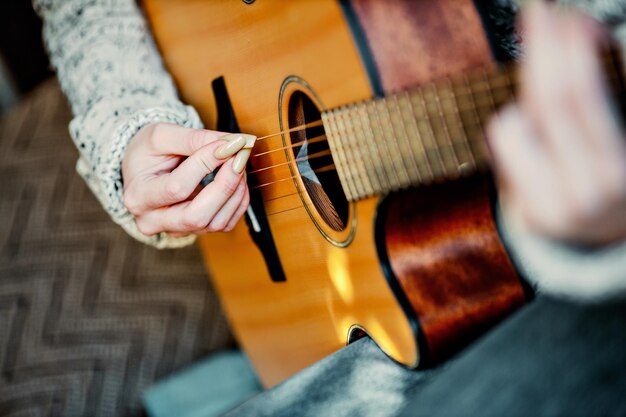 Chica joven con uñas largas toca la guitarra acústica en casa Adolescente se sienta en el sofá en la habitación y aprende a tocar la guitarra