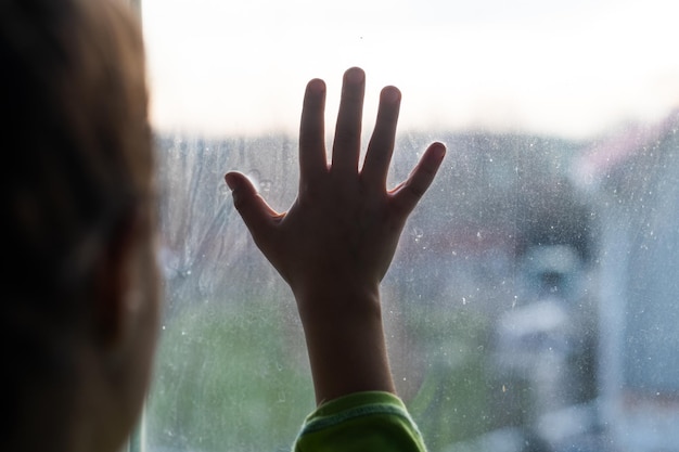 Chica joven en la ventana con las manos presionadas contra la ventana, pensativa o con ganas de salir