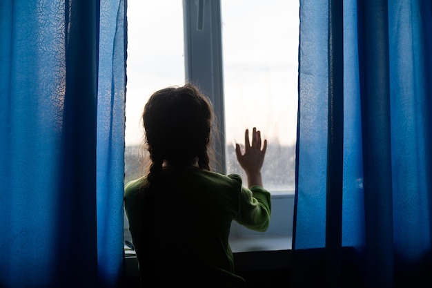 Foto chica joven en la ventana con las manos presionadas contra la ventana, pensativa o con ganas de salir