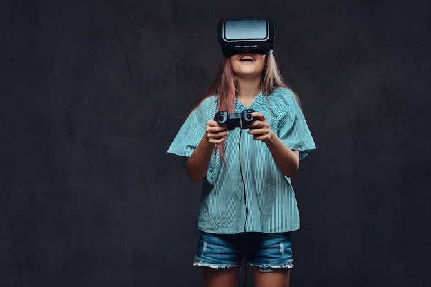 Chica joven vestida casual jugando el juego con el joystick y gafas de realidad virtual. Aislado en un fondo de textura oscura.