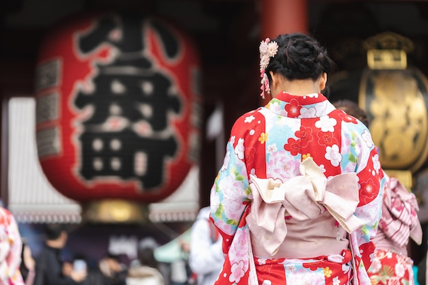 Chica joven vestida con un kimono japonés parado frente al templo Sensoji en Tokio,