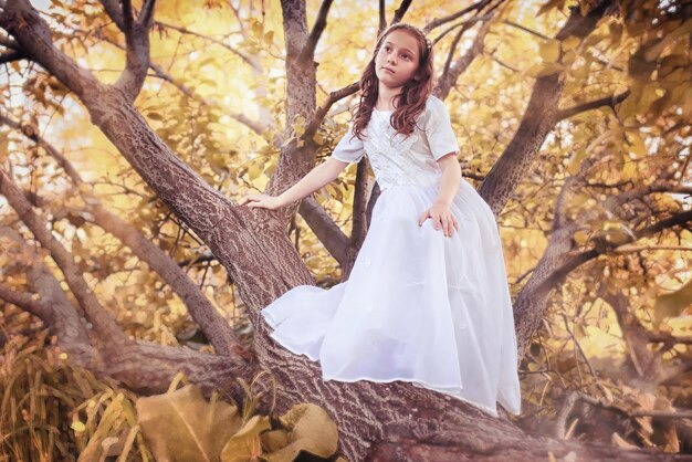 Chica joven en un vestido blanco contra un árbol en otoño