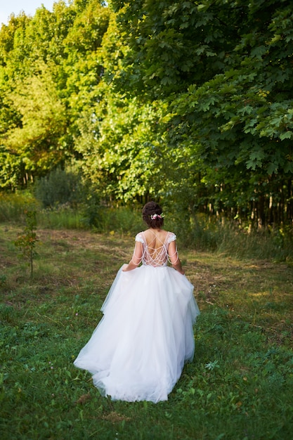 Chica joven en un vestido blanco en el prado. Mujer en un vestido largo hermoso que presenta en el jardín.