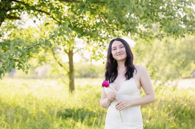Chica joven en vestido blanco con tulipanes rosas en el parque de primavera