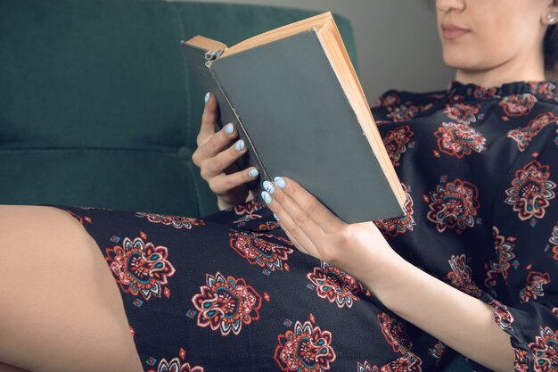 Chica joven en un vestido leyendo un libro sentado en un sofá