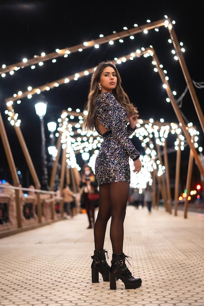 Chica joven en un vestido de moda con lentejuelas en las luces de navidad de la ciudad