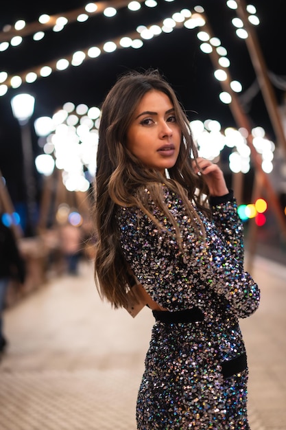 Chica joven en un vestido de moda con lentejuelas en las luces de navidad de la ciudad