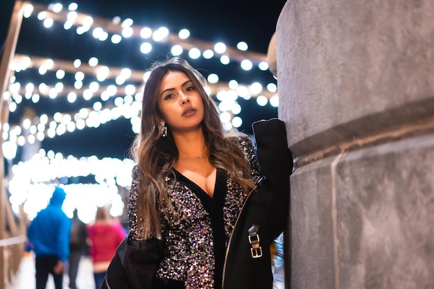 Chica joven en un vestido de moda con lentejuelas en las luces de navidad de la ciudad