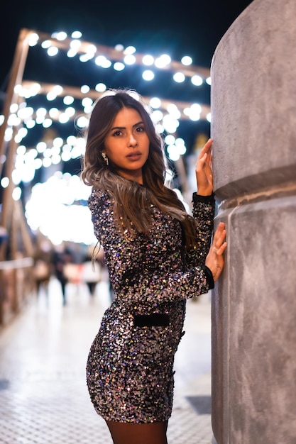 Chica joven en un vestido de moda con lentejuelas en las luces de navidad de la ciudad