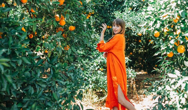 Chica joven en vestido naranja está mirando a la cámara en jardín naranja