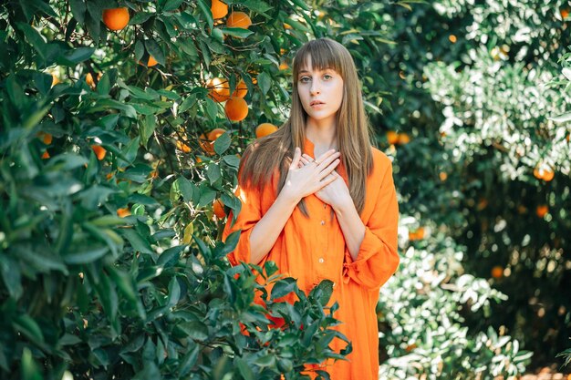 Chica joven en vestido naranja está mirando a la cámara poniendo las manos en la cintura en el jardín naranja