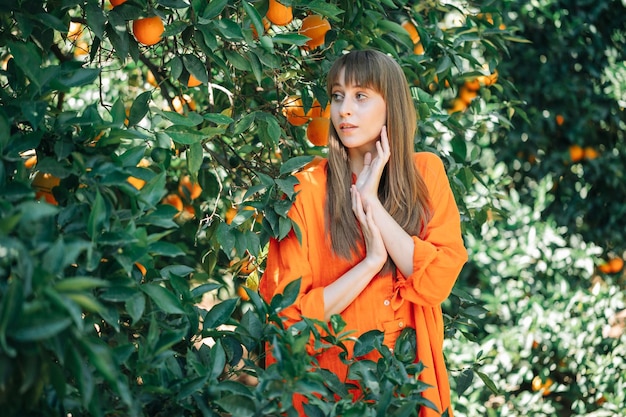 Chica joven con vestido naranja posa para la cámara mirando hacia otro lado en el jardín naranja