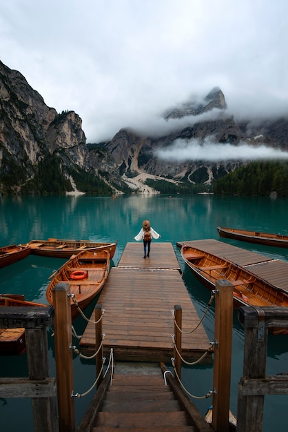 Chica joven viajero con sombrero y mochila vintage en el embarcadero del lago di Braies rodeado por las montañas de los Alpes italianos