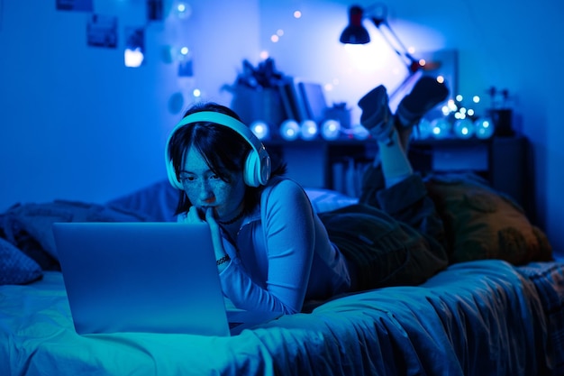 Chica jugando en la computadora portátil en su cuarto oscuro