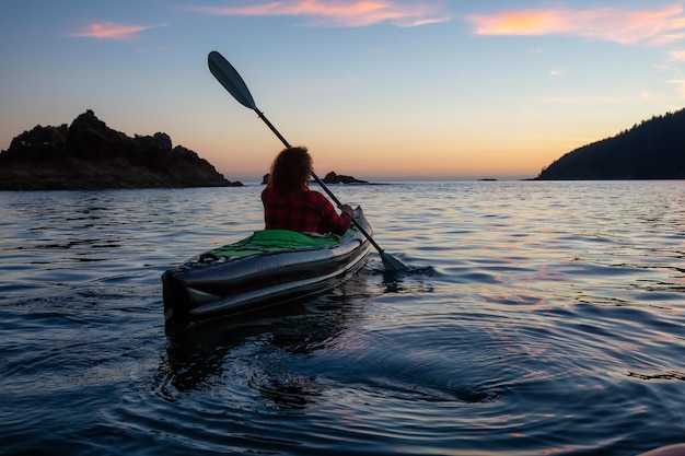 Chica en kayak en el Océano Pacífico durante un atardecer de verano nublado