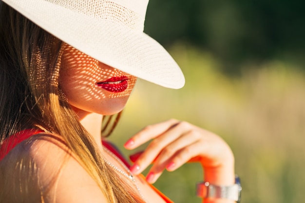 Foto chica de labios seductores con lápiz labial rojo, la mitad más grande de la cara cubre un elegante sombrero