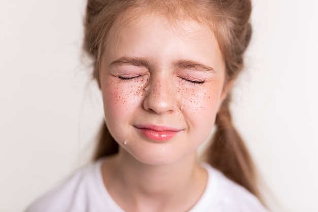 Chica con lágrima. Niña bonita extremadamente molesta cerrando los ojos y llorando con grandes lágrimas