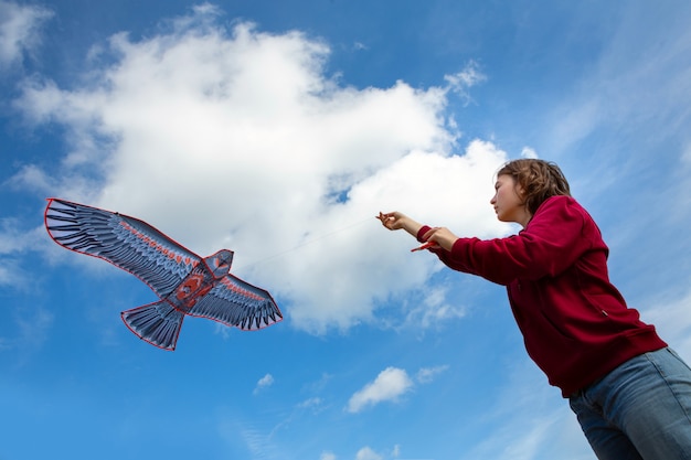 Chica lanza una cometa. Cometa voladora Cometa en forma de águila. Cielo azul con nubes.