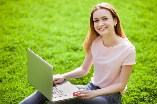 Chica con laptop sentada en la hierba y sonriendo