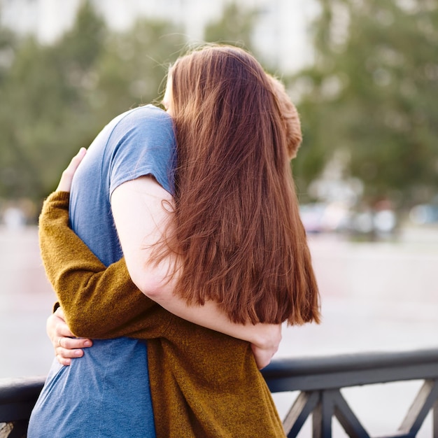 Chica con largo y grueso oído oscuro abrazando a un chico pelirrojo en el puente amor adolescente al atardecer