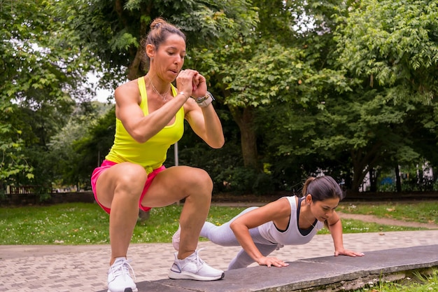 Chica latina haciendo deporte en un parque de la ciudad, estilo de vida una vida sana, dos chicas haciendo estiramientos y sentadillas