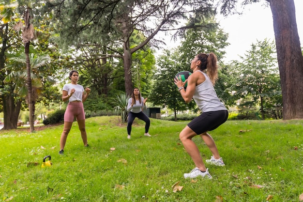 Chica latina haciendo ejercicio y deporte en un parque verde, instructor enseñando a los estudiantes con ejercicios de pesas y una pelota pesada