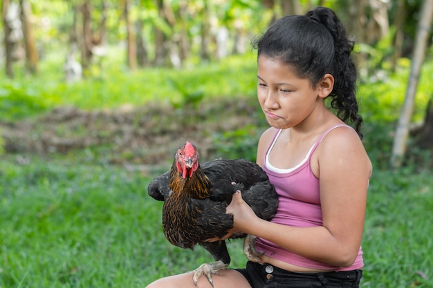 Foto chica latina morena sosteniendo un pollo negro en sus manos mientras lo mira