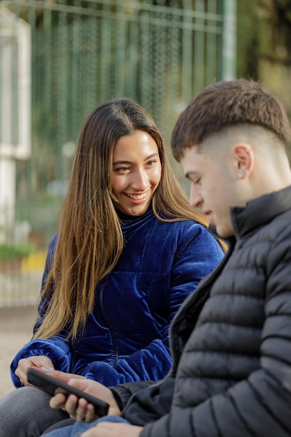 Una chica latina sonriente mirando a un tipo en un banco de la plaza con su novio