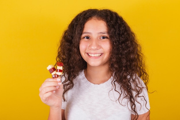 Chica latinoamericana afrobrasileña con cabello rizado sonriendo sosteniendo brochetas de queso y guayaba con aspecto apetitoso anhelando romeo y julieta dulce delicioso