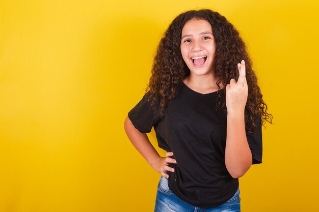 Chica latinoamericana brasileña para cabello afro fondo amarillo signo sonriente de suerte dedos cruzados torciendo deseando feliz