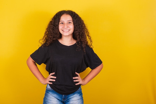 Chica latinoamericana brasileña con pelo afro fondo amarillo brazos y manos en la cintura feliz sonriendo alegre empoderada confiada