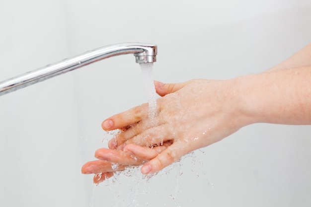 Chica lava sus manos bajo el agua con jabón. Desinfección de manos