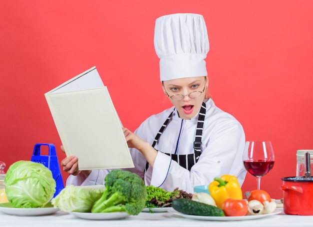 Chica lee el libro mejores recetas culinarias. Concepto de educación culinaria. La mujer con sombrero y delantal lo sabe todo sobre las artes culinarias. Mejora la habilidad de cocinar. Experto culinario. Cocinero de la mujer que cocina la comida sana.