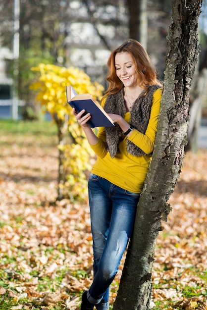 Chica lee un libro en el parque de otoño entre las hojas amarillas