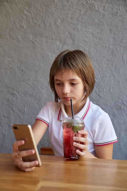 Chica leyendo información sobre el teléfono bebiendo cóctel helado rojo en la mesa del café