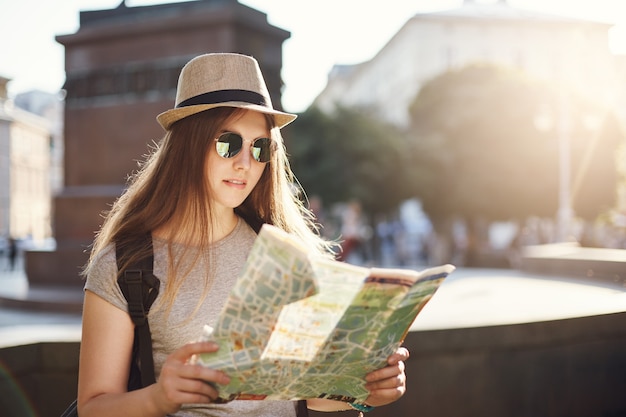 Chica leyendo un mapa viajando por el mundo, sentada en una ciudad europea con sombrero. Hacer turismo es una gran inversión.