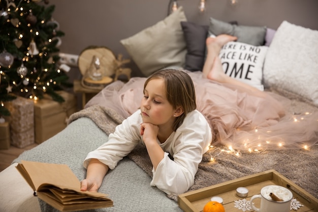 Chica con un libro acostado en la cama, desayuno en la cama