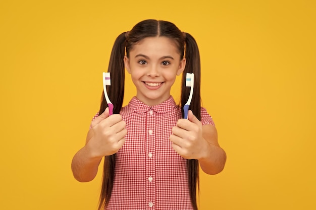 Chica limpia sus dientes con un cepillo Retrato hermosa adolescente sosteniendo cepillo de dientes cepillarse los dientes aislado sobre fondo amarillo Concepto de salud dental Adolescente feliz emociones positivas y sonrientes