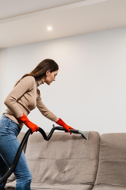 La chica limpiadora está limpiando el sofá con una máquina de extracción para muebles tapizados de limpieza en seco