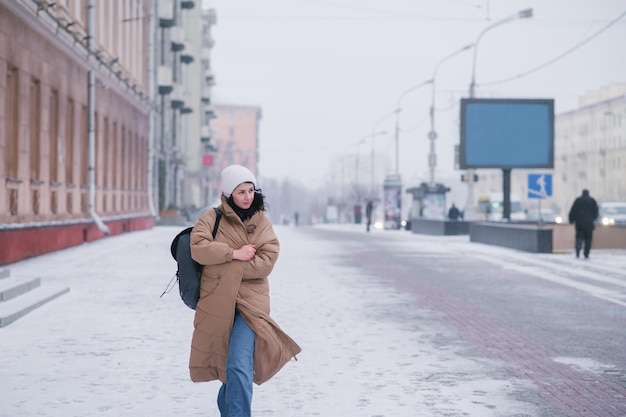 Foto una chica linda con un abrigo está caminando por la ciudad en mal tiempo frío llevando una mochila